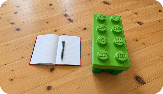 Notesbog og en stor grøn LEGO-klods på et træbord